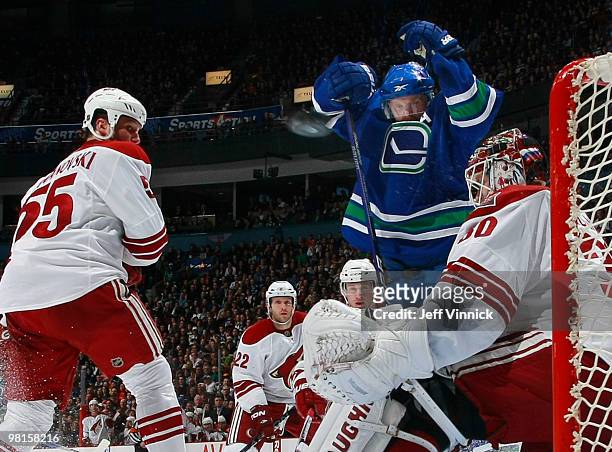 Henrik Sedin of the Vancouver Canucks and Ed Jovanovski of the Phoenix Coyotes look on as the puck is shot to the left of Ilya Bryzgalov during their...