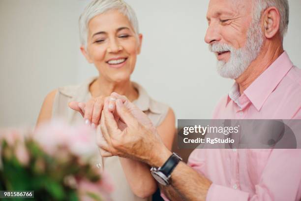 content mature man putting an engagement ring on woman's finger - putting ring on finger stock pictures, royalty-free photos & images