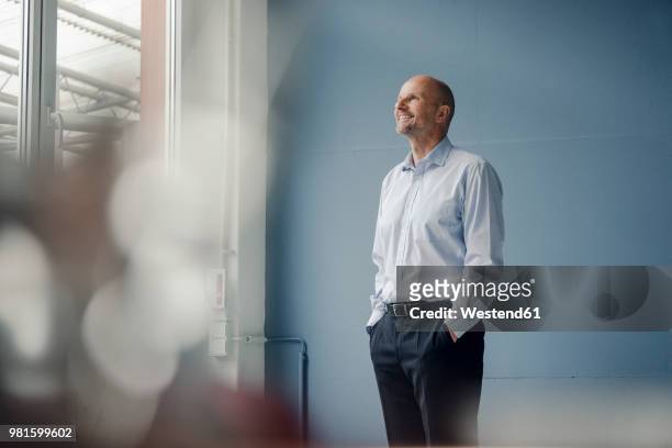 smiling mature businessman looking out of window - three quarter length stock pictures, royalty-free photos & images