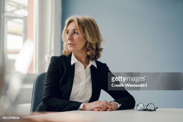 senior businesswoman sitting at table looking sideways - leaning stock pictures, royalty-free photos & images