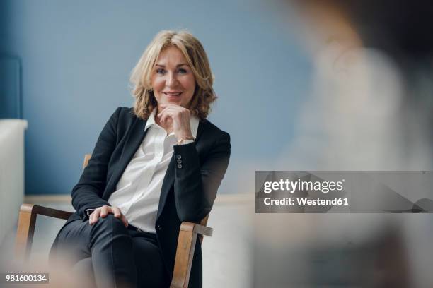 portrait of smiling senior businesswoman sitting in chair - autorità foto e immagini stock