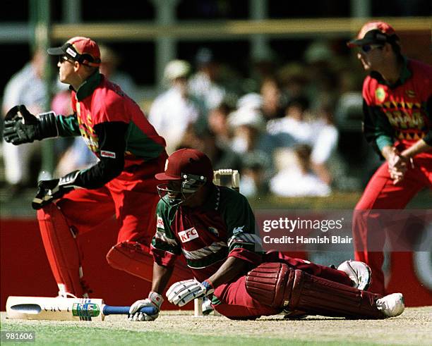 Brian Lara of West Indies falls over whilst sweeping during his innings of 83 not out as Zimbabwe wicketkeeper Andy Flower looks on during the...