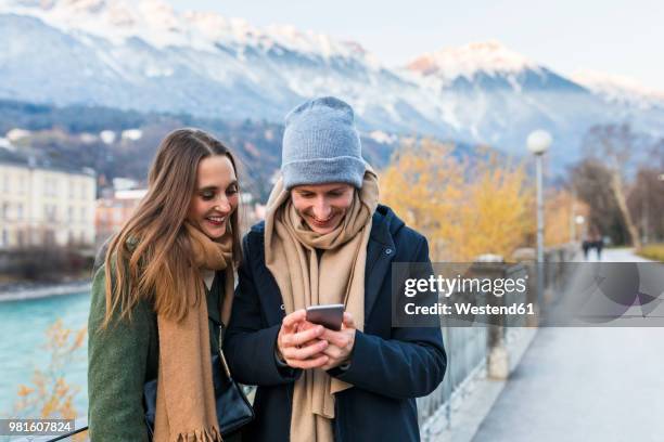 austria, innsbruck, happy young couple looking at cell phone - winter travel stock-fotos und bilder