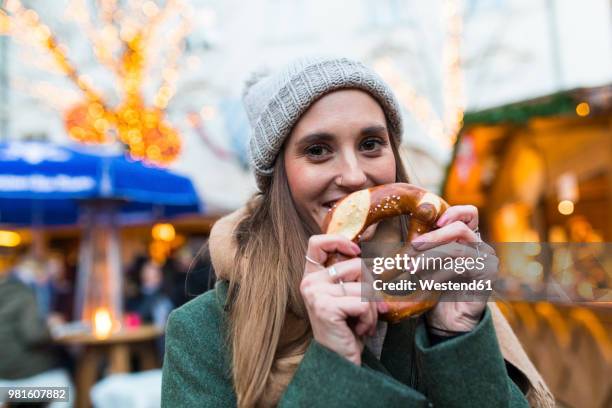 portrait of smiling young woman with pretzel at christmas market - breze stock-fotos und bilder