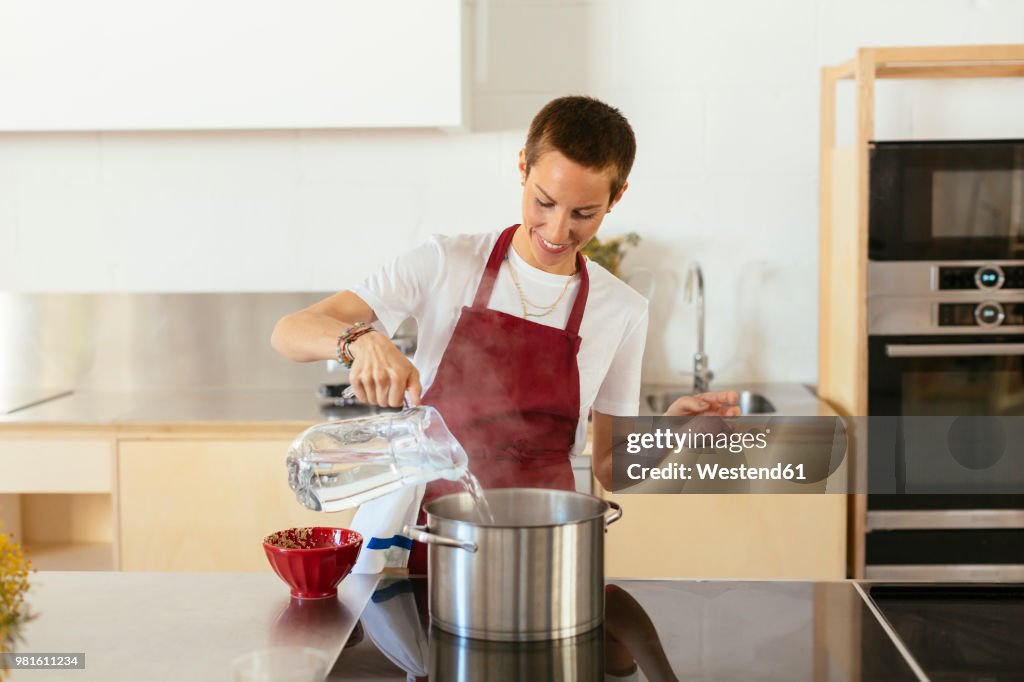 Woman boiling water in cooking pot in kitchen