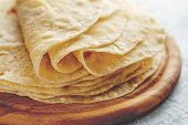 Stack of homemade wheat flour tortilla wraps on wooden cutting board.