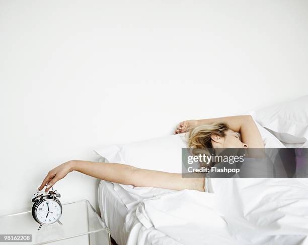woman reaching to turn alarm clock off - junge frau uhr stock-fotos und bilder