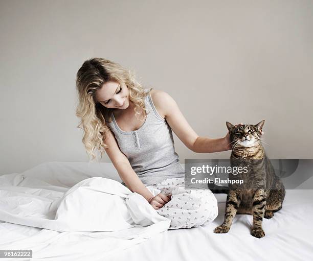 woman sitting on bed stroking her cat - vêtement de nuit photos et images de collection