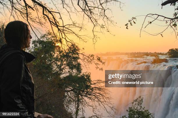 Zambia. Victoria Falls. Sambesi river. Girl admires Victoria Falls at sunset.