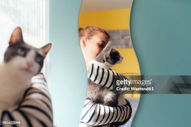 woman holding a gray cat next to a mirror at home - bedroom mirror stock-fotos und bilder