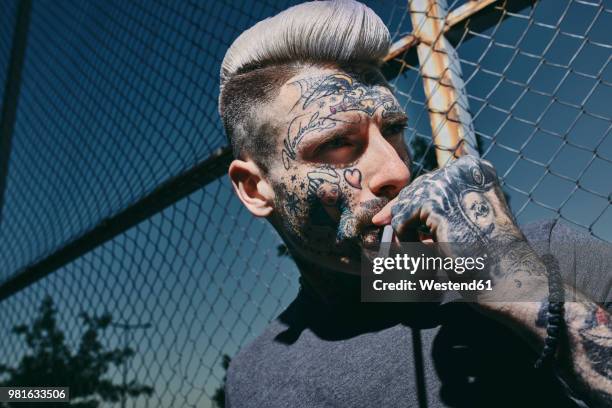 portrait of tattooed young man smoking a cigarette at wire mesh fence - anti smoking bildbanksfoton och bilder