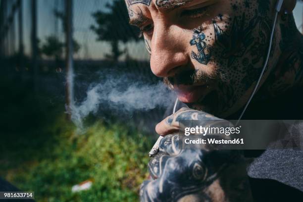 close-up of tattooed young man with earbuds smoking a cigarette - anti smoking bildbanksfoton och bilder