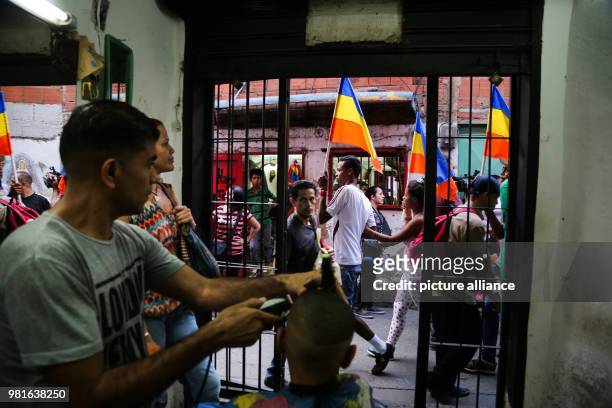 March 2018, Venezuela, Caracas: Supporters of opposition candidate Henri Falcon walking by a hair salon carrying national flags during a visit by...