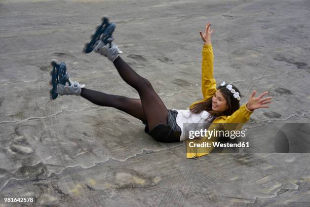 smiling woman with inline skates falling on ground - maillot de sport stockfoto's en -beelden