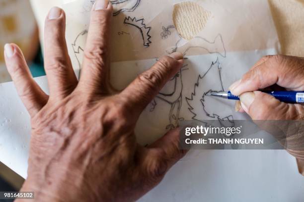 This picture taken on June 20, 2018 shows retired Vietnamese English teacher Nguyen Thanh Tam making paper cutouts as he creates a model of Zabivaka,...