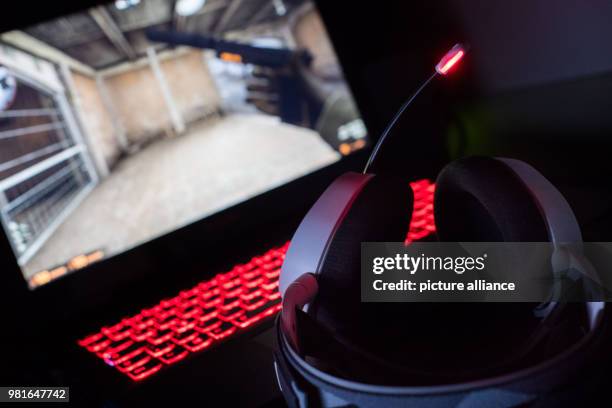 March 2018, Germany, Munich: Gaming headphones lie on a gaming laptop. On the screen a shooter can be seen. Photo: Lino Mirgeler/dpa