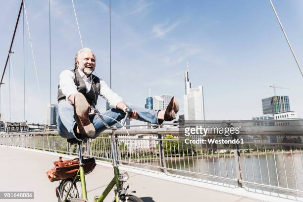 playful mature man on bicycle on bridge in the city - spensieratezza foto e immagini stock