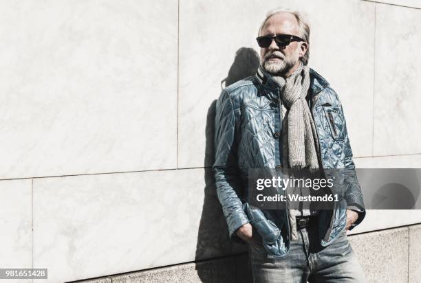 portrait of fashionable mature man wearing sunglasses leaning against a wall - minder verzadiging stockfoto's en -beelden