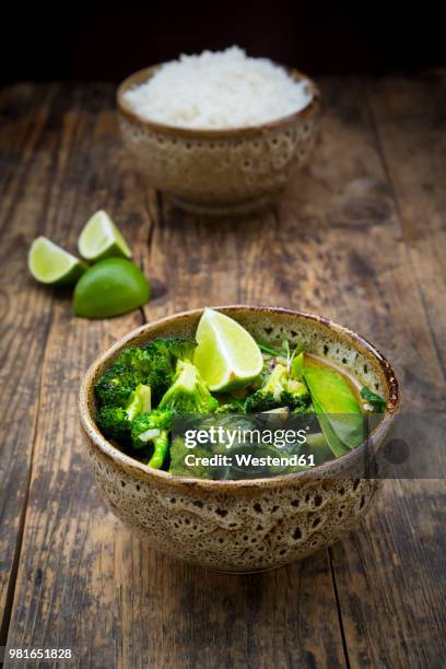 green thai curry with broccoli, pak choi, snow peas, baby spinach, lime and bowl of rice in the background - fresh baby spinach stock-fotos und bilder