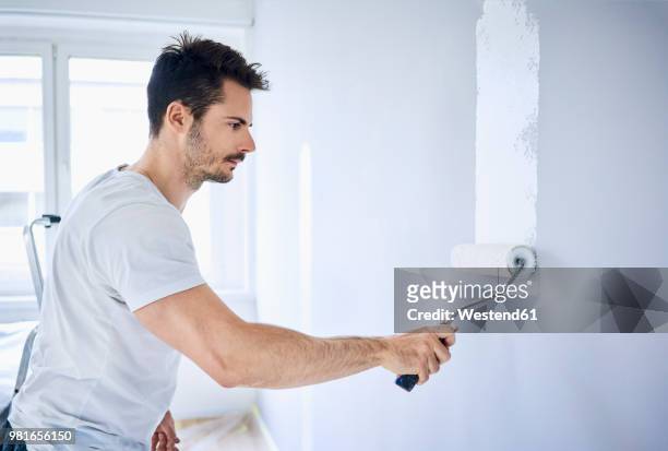 man painting wall in apartment - white paint roller stock pictures, royalty-free photos & images