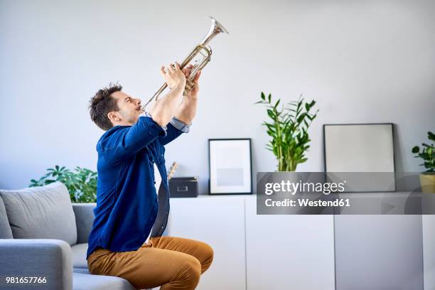 man sitting on couch playing trumpet - brass instrument stock pictures, royalty-free photos & images