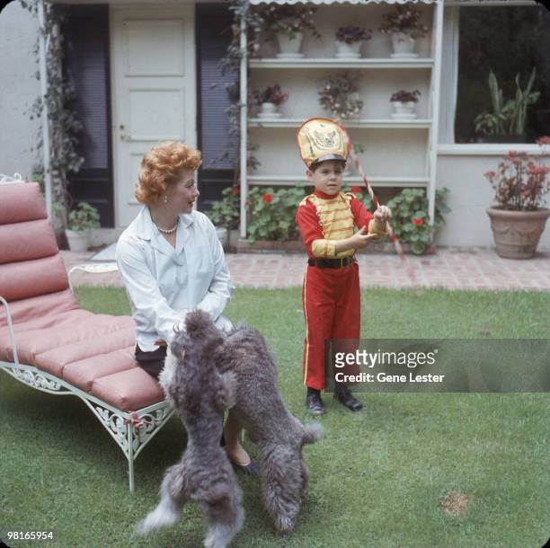 American actress and comedienne Lucille Ball watches as her son Desi Arnaz Jr, dressed as a drum major, twirls a baton in the back yard of their...