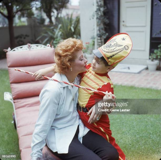 American actress and comedienne Lucille Ball kisses her son Desi Arnaz Jr, who is dressed as a drum major with a baton, in the back yard of their...