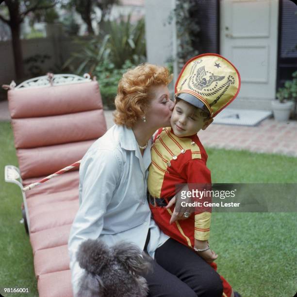 American actress and comedienne Lucille Ball kisses her son Desi Arnaz Jr, who is dressed as a drum major with a baton, in the back yard of their...