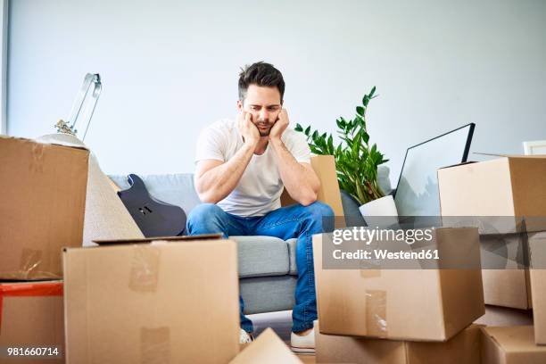 frustrated man sitting on couch surrounded by cardboard boxes - man on the move stock pictures, royalty-free photos & images