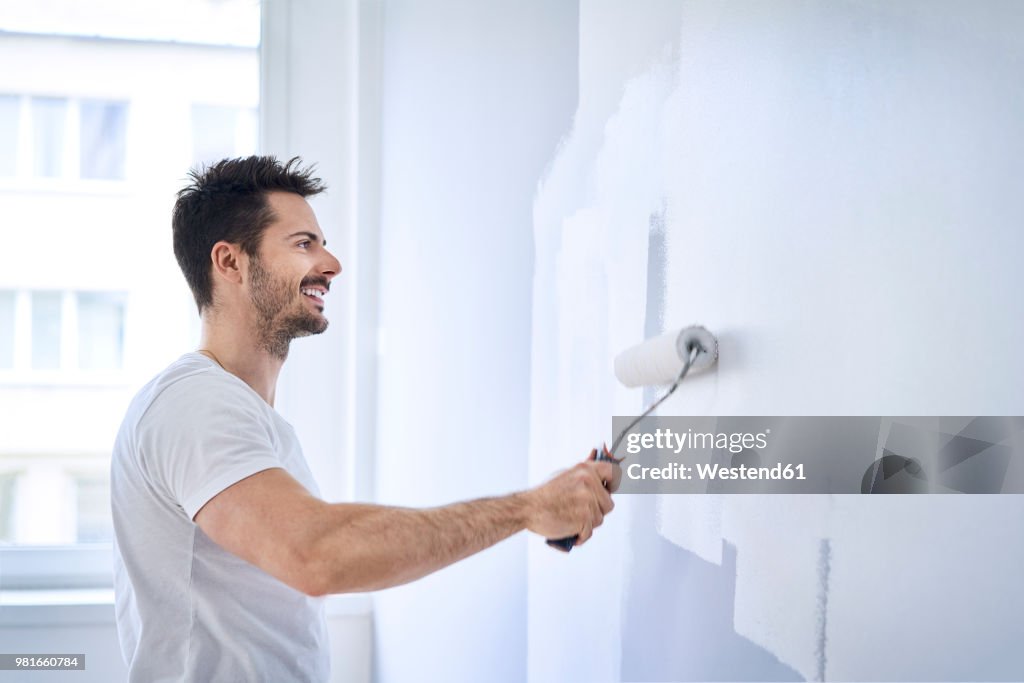 Smiling man painting wall in apartment