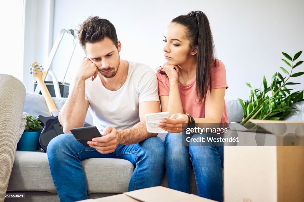 Serious couple sitting on couch in new home checking bills