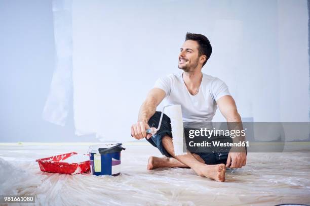 smiling man sitting in new apartment taking a break from painting - white paint roller stock pictures, royalty-free photos & images