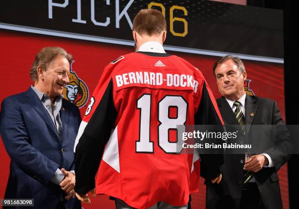 Jacob Bernard-Docker puts on an Ottawa Senators jersey onstage after being selected twenty-sixth overall by the Ottawa Senators during the first...