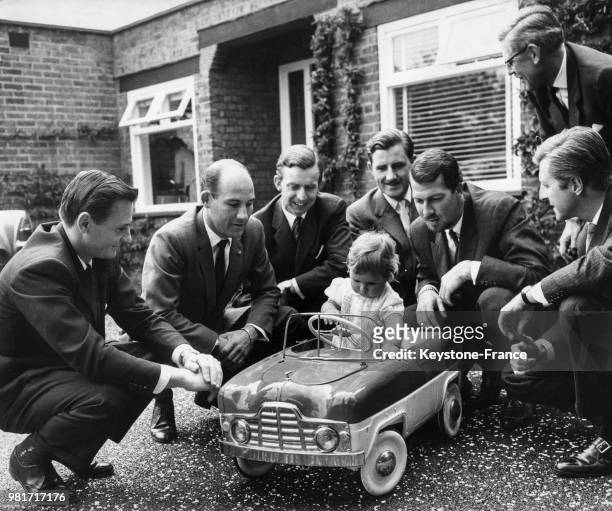 Damon Hill, 10 mois, le jour de son baptême, au volant d'une voiture miniature, entouré de Bruce McLaren, Stirling Moss, Tony Brooks, Graham Hill,...