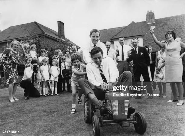 Lors de la fête donnée pour sa victoire à Indianapolis, Graham Hill et son fils Damon Hill poussent le tracteur conduit par Jim Clark à Mill Hill en...