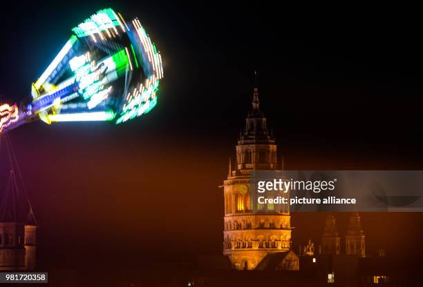 April 2018, Germany, Mainz: The gondola of a roundabout moves in front of the Mainz Cathedral and a car drives along the Theodor-Heuss-Bridge. The...