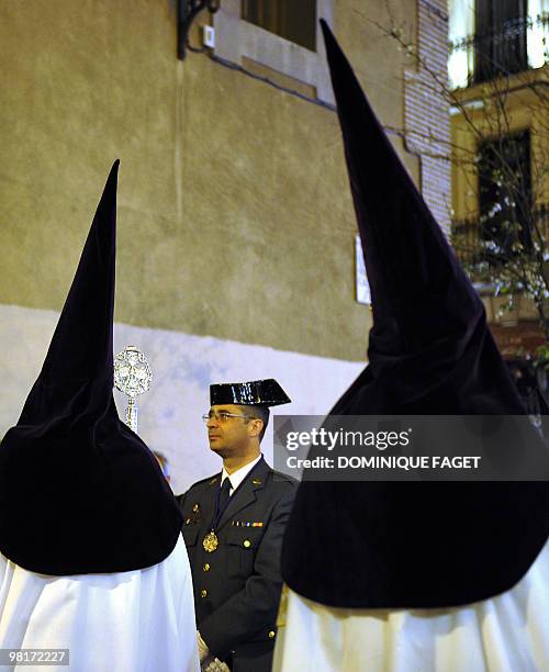 Penitents walk past a police officer of the Guardia Civil as they take part in the ''Nuestro Padre Jesus de la Salud" brotherhood procession during...