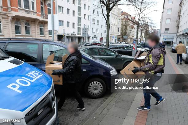 April 2018, Germany, Hannover: Two police officers in civil clothing carrying boxes of confiscated documents to a car during a raid of the Kurdish...