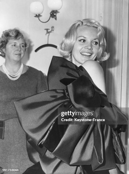 Carroll Baker porte la robe 'Milano', un fourreau en velours noir avec manteau cape orné de coques en zibeline noire et velours noir, lors d'un...