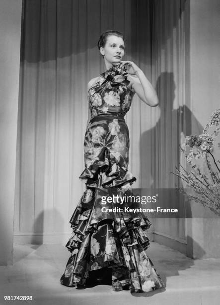 Mannequin présentant la robe du soir à volants de Maggy Rouff 'Les oeillets' en taffetas gris ornée d'oeillets roses et blancs, le 19 février 1947.