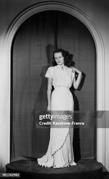 Mannequin présentant le modèle 'Pol Roger' de Jacques Costet : une robe blanche longue plissée pour le soir, en 1947.