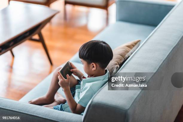 chinese jongen met behulp van slimme telefoon in de woonkamer - child playing in room stockfoto's en -beelden