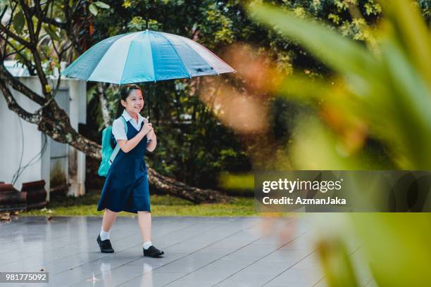 little chinese girl coming home from school with an umbrella - coming back stock pictures, royalty-free photos & images