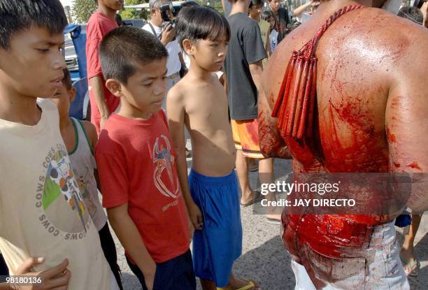 Children look on as a devotee in the city of San Fernando, Pampanga in the Roman Catholic Philippines, takes part in the annual Maundy Thursday, the...