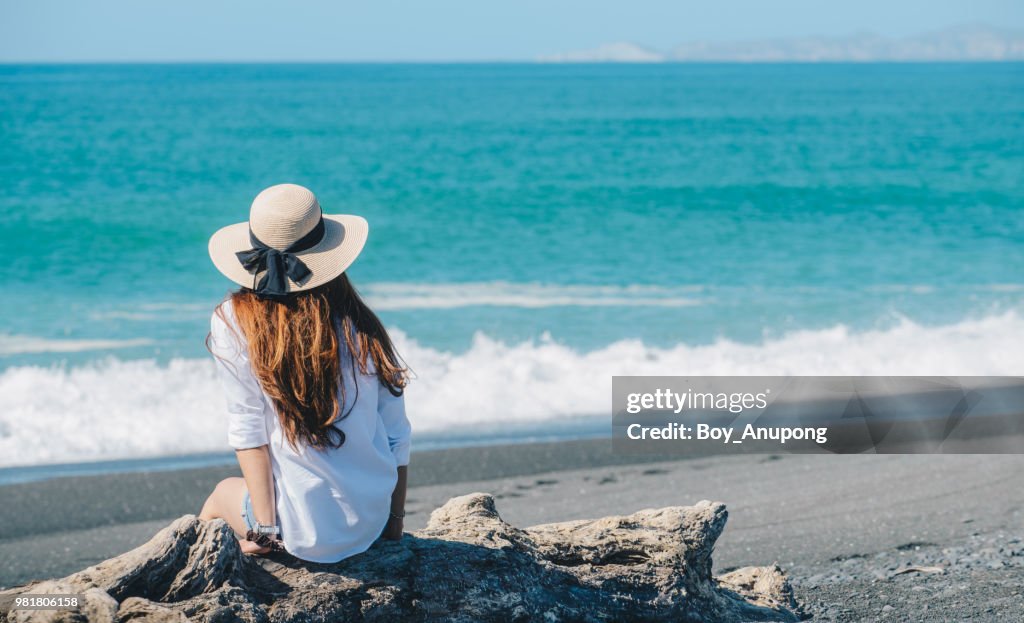Back view of Asian women travelling and relaxing at the black sand beach of Napier town in New Zealand.