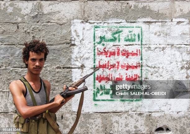 Yemeni fighter from the Amalqa Brigades loyal to the Saudi-backed government stands pointing a Kalashnikov assault rifle towards a Huthi-rebel banner...