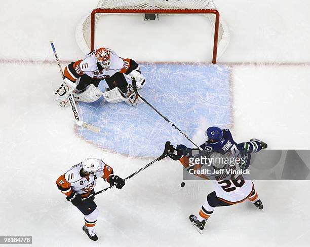 Mark Streit of the New York Islanders plays the puck as teammate Matt Moulson checks Aaron Rome of the Vancouver Canucks in front of Dwayne Roloson...