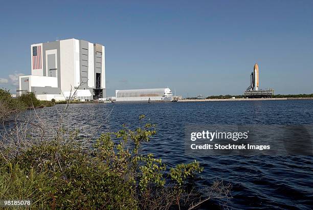 viewed across the basin, space shuttle atlantis crawls toward the launch pad. - nasa kennedy space centre stock pictures, royalty-free photos & images