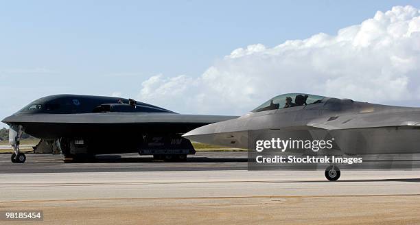 an f-22 raptor taxis while a b-2 spirit waits for clearance. - f 22 raptor stock-fotos und bilder