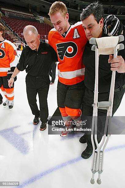 Jeff Carter of the Philadelphia Flyers with his broken left foot in a cast is helped to the stage for the annual team photo by athletic...